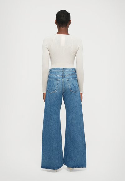 Ribbed cream long-sleeve top with a back cutout, paired with high-waisted, wide-leg blue denim jeans featuring two back pockets.