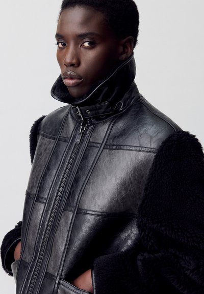 Chaqueta de cuero negra con cuello alto, que presenta paneles texturizados, cierre de cremallera y lujosos acentos de piel de pelo negro en las mangas.