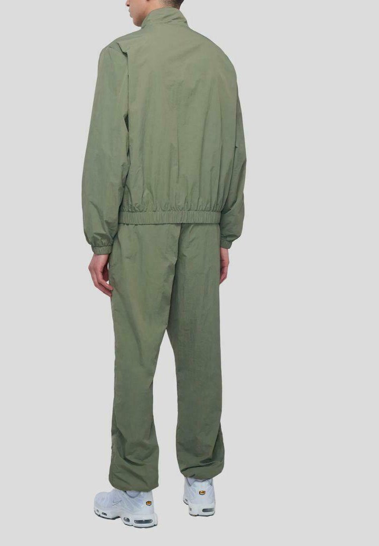 Olivgrüner Trainingsanzug mit elastischen Bündchen und Bund, der ein minimalistisches Design aufweist. Getragen mit weißen Sneakers, zeigt eine schlichte Rückansicht.