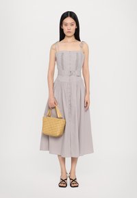 Vaaleanharmaa mekko, jossa on ohuita olkaimia, istuva bodice, nappilista edessä ja liehuva hame. Pitelee käsissä kudottua keltaista laukkua. Mustat remmi-sandaalit.