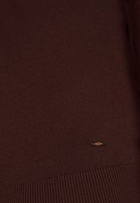 Maglione lavorato a maglia bordò realizzato in tessuto a coste. Presenta una discreta toppa con logo sul lato inferiore e una finitura testurizzata.