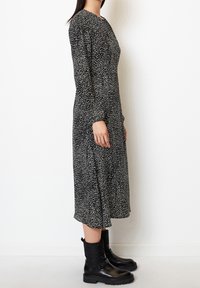 Schwarzes Langarmkleid mit weißem gepunktetem Muster, runder Ausschnitt, Knielänge; kombiniert mit schwarzen Knöchelstiefeln mit gestepptem Detail.