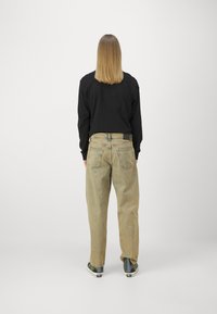 Black long-sleeve shirt paired with loose, beige denim jeans. Jeans feature a high waist, five pockets, and a light distressed texture.