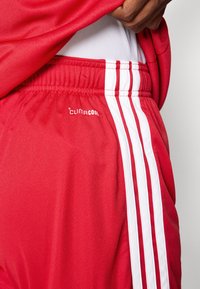 Κόκκινα αθλητικά σορτς από λείο ύφασμα, με ελαστική μέση, λευκές πλαϊνές ρίγες και λογότυπο "Climacool" στο μπροστινό μέρος.