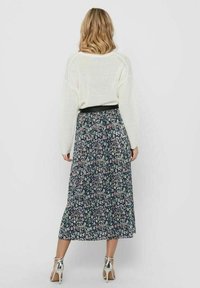 Maglione bianco a maglia con maniche ampie abbinato a una gonna maxi a fiori in tessuto scuro, caratterizzata da piccoli fiori colorati e una cintura nera.