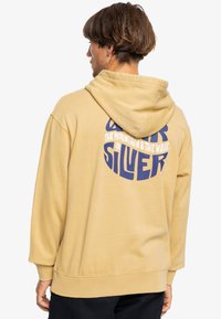 Yellow hooded sweatshirt with a relaxed fit, featuring a large blue graphic text on the back. Soft fabric with ribbed cuffs and hem.