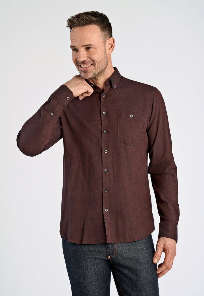 Camisa de manga larga color granate con botones, cuello puntiagudo, un bolsillo en el pecho y botones en contraste, combinada con jeans oscuros.