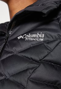 Svart Columbia Titanium pufferjakke med quiltet design, som har glidelås og brodert logo på brystet.