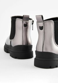Metallisch silberne Knöchelstiefel mit schwarzen elastischen Seiteneinsätzen, Gummisohlen und bärenförmigen Akzenten auf der Rückseite. Rundes Ze design.
