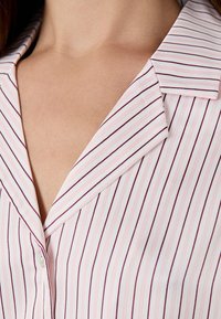 Witte blouse met verticale roze en donkerpaarse strepen, voorzien van een notch kraag en een knoopdetail bij de halslijn. Soepele textuur.