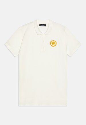 White polo shirt made of cotton, featuring a yellow embroidered lion emblem with a laurel wreath on the left chest. Short sleeves and collar.