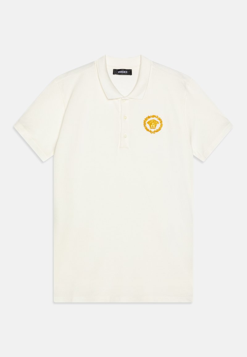 Camisa polo blanca de algodón, con un emblema de león bordado en amarillo y una corona de laurel en el lado izquierdo del pecho. Mangas cortas y cuello.