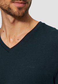 Tmavomodré tričko s výstrihom do V vyrobené z jemnej bavlny s krátkymi rukávmi. Obsahuje jemne vyšívané logo s.Oliver na ľavej strane hrudi.