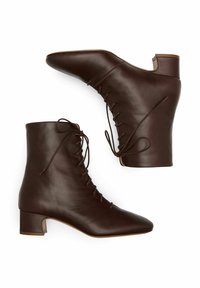 Brązowe skórzane botki za kostkę z zaostrzonym noskiem, sznurowane z przodu i o niskim, szerokim obcasie. Gładka faktura i subtelne detale szwów.