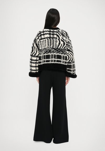 Un pull en tricot noir et blanc à motifs, avec une coupe confortable, des poignets et un ourlet côtelés, associé à un pantalon large noir ample.