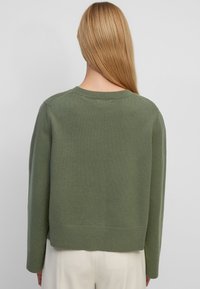 Pull vert tricoté avec un col rond, épaules tombantes et ourlet côtelé. Texture douce, coupe décontractée et manches de longueur moyenne.