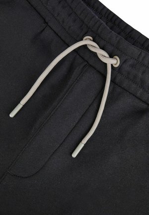Black drawstring shorts feature a textured fabric, elastic waistband, and a light gray drawstring with metal tips. Includes a front pocket.