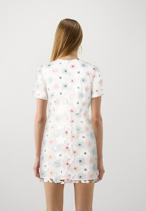 Robe blanche avec des appliqués floraux en rose, bleu et or, manches courtes, et une fermeture à boutons à l'arrière. Texture transparente et longueur au genou.