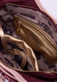 Interno di borsa in suede bordeaux con una tasca con zip dorata etichettata "SHOP!" e un rivestimento in tessuto beige liscio con un design a scritta.