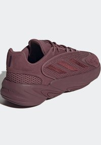 Burgundy idrottssko med nät- och mockaovandel, böjd sula, framträdande snörning och tre-stripes logotyp på sidan.