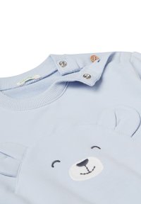 Světlomodré dětské body s kovovými knoflíky na rameni a aplikací usmívající se medvědí tváře se ušima na přední straně.