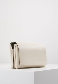 Borsa a pochette in ecopelle color crema con chiusura a pattina, forma arrotondata e cuciture in evidenza. Presenta una cerniera su un lato.