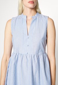 Vestido sem mangas azul claro com riscas brancas verticais, colarinho mandarim e fecho de botão à frente. A saia tem pormenores franzidos.