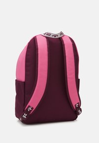 Ryggsäck med mörkt vinröd kropp och ljusrosa remmar. Har en liten sidoficka och ett märkt övre handtag. Slät tygstruktur.