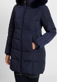 Navy puffer coat with a zip closure, featuring a fur-lined hood, quilted design, side pockets, and ribbed cuffs.