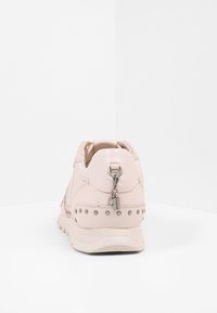 Světlé růžové tenisky s hladkým koženým svrškem, dekorativními hřebíky na patě a připevněným kovovým přívěskem.