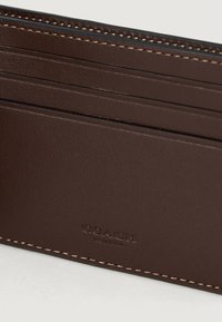Cardholder din piele maro cu multiple sloturi și logo-ul embosat "COACH NEW YORK", având cusături detaliate pe margini.