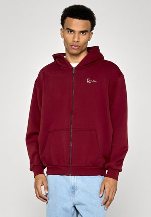 Bordeaux zip-up hoodie i mjukt tyg, med en stor framficka, ribbade muddar och huva med dragsko. Liten vit logotyp på bröstet.
