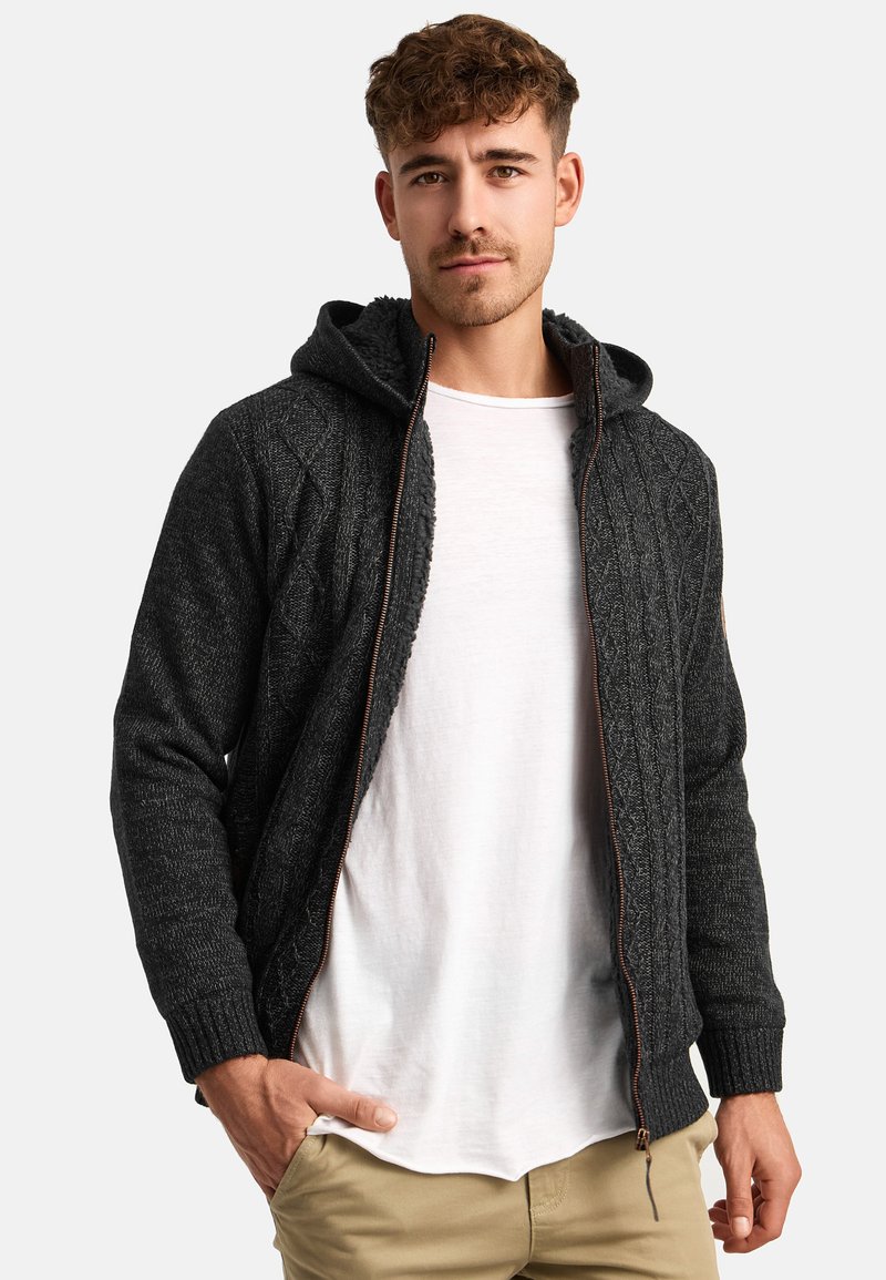 Ciemnoszary, dziany hoodie z teksturowanym wzorem, z zamkiem z przodu i ściągaczami na mankietach. Noszony na białej koszuli przez modela z krótkimi włosami.