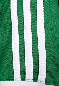 Maillot de sport vert avec des bandes blanches sur les côtés. Le tissu est texturé, présentant des coutures verticales et un motif tricoté respirant.