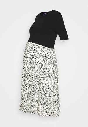 Czarna dopasowana krótka bluzka z krótkim rękawem w połączeniu z białą, wysokim stanem, midi spódnicą z małymi nieregularnymi czarnymi plamkami.