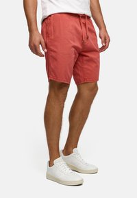 Røde bomullsshorts med elastisk midje og snor, sidelommer og avslappet passform. Sammen med hvite sneakers.