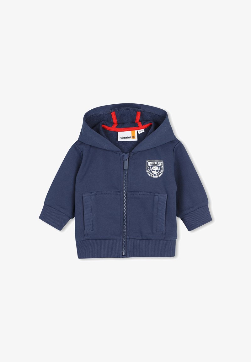 Sweat à capuche bleu marine pour tout-petit avec fermeture éclair à l'avant, deux poches, poignets côtelés, bordure de capuche intérieure rouge et logo Timberland blanc sur la poitrine.