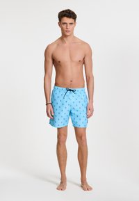 Light blue swim shorts with a drawstring waist, featuring a pattern of small dark blue leaf-like shapes. Made from a smooth, quick-drying fabric.