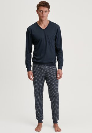 Haut à manches longues bleu marine en V avec une poche poitrine, associé à un pantalon de pyjama à motifs avec des pois blancs sur un fond sombre.