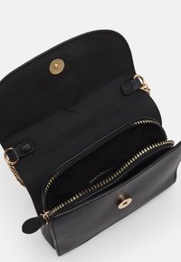 Musta nahkakäekott, millel on kuldne klamber. Siseosa on kaetud musta kangaga ja seal on lukuga tasku kuldsete metalldetailidega.