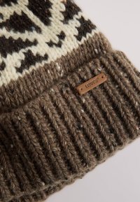 Brown knitted hat with a geometric pattern in cream and dark tones, featuring a ribbed cuff and a small brown leather label.