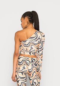 Top crop de uma manga e leggings combinando em um padrão ondulado de cores pêssego, preto e menta; material elástico com acabamento suave.