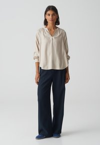 Lichtbeige blouse met een V-hals en lange mouwen, gecombineerd met donkerblauwe wijde broeken. Soepele stof met een ontspannen pasvorm.