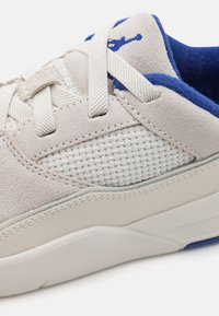 Lys grå sneaker med en kombinasjon av semsket skinn og mesh-materiell, med blå aksenter, flate snørebånd og en teksturert hvit såle.