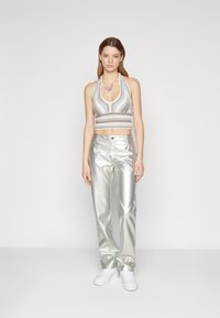 Halter-neck strikket cropped topp i hvit og sølv med stripete mønster, kombinert med metallisk sølvrett bukser og hvite joggesko.
