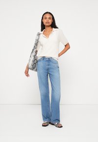Svetlo bež majica s kratkimi rokavi in ovratnikom, v kombinaciji s svetlo modrimi visokimi flare jeans hlačami. Dodatna oprema: torbica z vzorcem kačje kože.