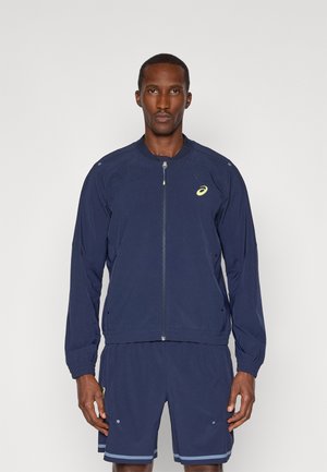 Navy athletic jacket with a zip front, relaxed fit, breathable fabric, and side pockets. Features a logo on the chest and shoulder.