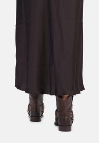 Brown leather ankle boots with buckles, worn with a long black skirt, displaying a smooth fabric texture and a flowing silhouette.