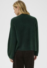 Ciemnozielony, oversize'owy sweter dzianinowy z okrągłym dekoltem i ściągaczami, charakteryzujący się miękką teksturą i lekko skróconym połączeniem.