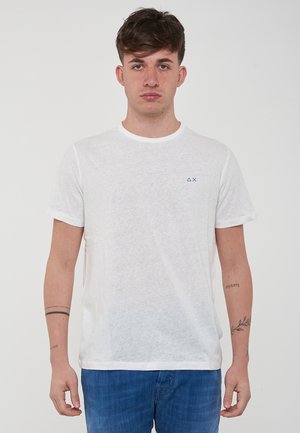 T-shirt bianco a maniche corte con collo rotondo, realizzato in tessuto leggero, con un piccolo logo blu sulla parte sinistra del petto.